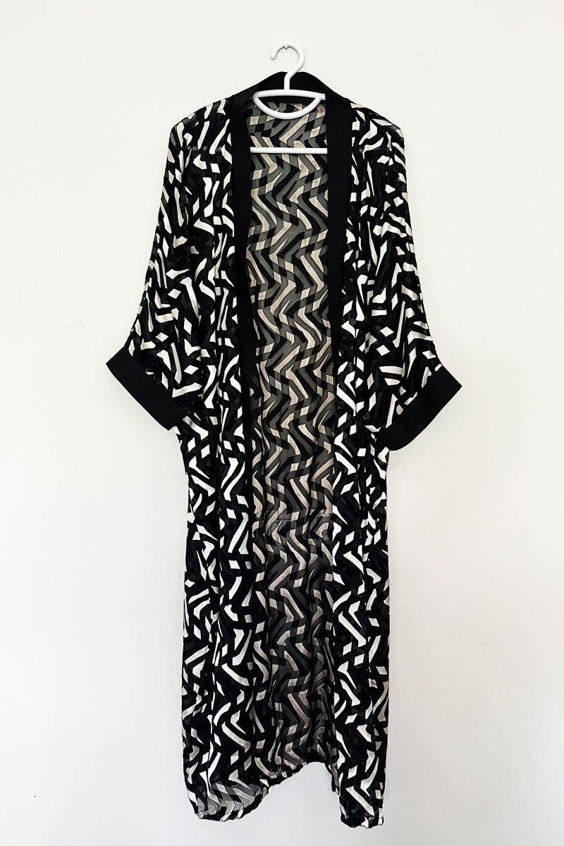 Elevate your style with our chic black and white Brochia kimono, featuring a striking geometric pattern. This lightweight and airy kimono is perfect for adding a touch of sophistication to any outfit. The open-front design, complemented by black trim, makes it an easy and versatile piece to layer over both casual and formal .